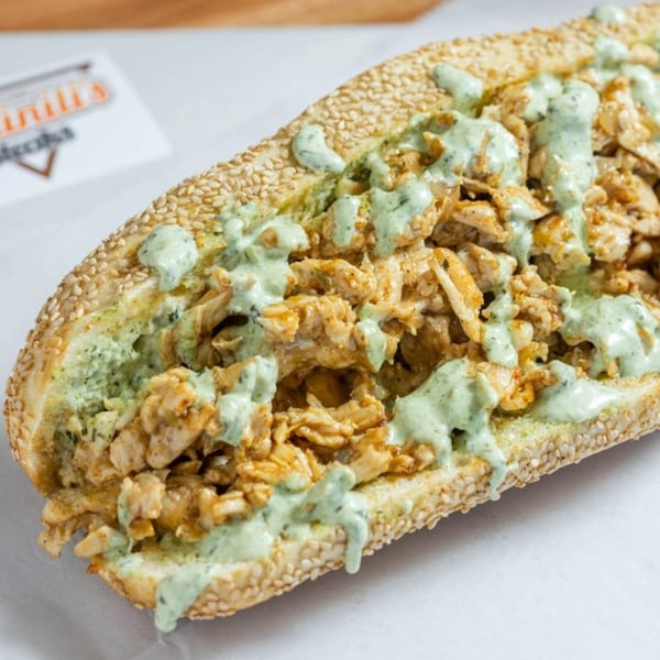 Ochinilis Steaks' chicken cheesesteak on a sesame seed roll, drizzled with green sauce.