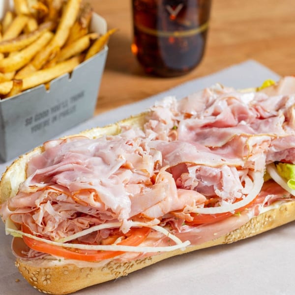Ochinilis Steaks' large Italian hoagie with fries and a drink on a wooden table.