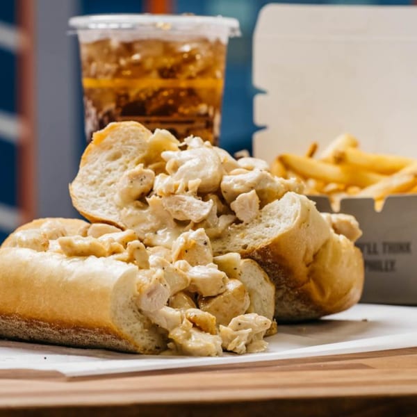 Ochinilis Steaks' chicken cheesesteak with fries and a drink on a wooden table.