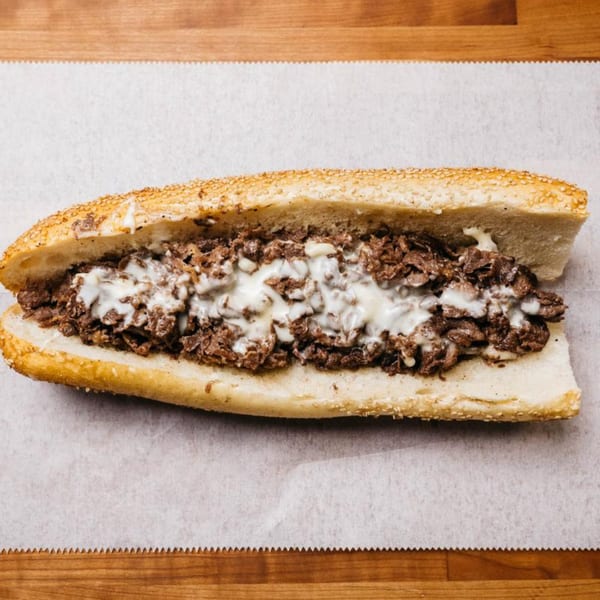 Ochinilis Steaks' cheesesteak, featuring thinly sliced steak and melted cheese on a sesame seed roll.