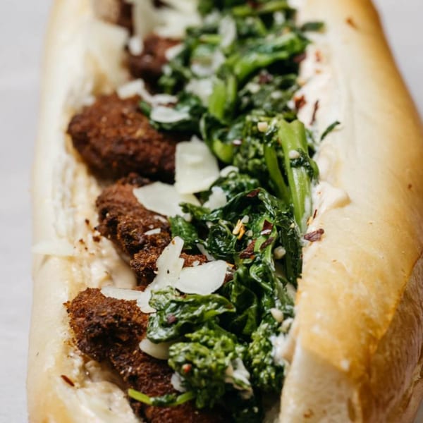 Close-up of an Ochinilis cheesesteak with dark meat, green vegetables, and white cheese in a bun.