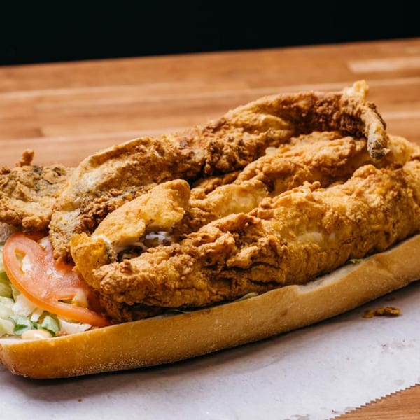 A crispy fried fish po'boy sandwich with lettuce and tomato on a wooden surface.